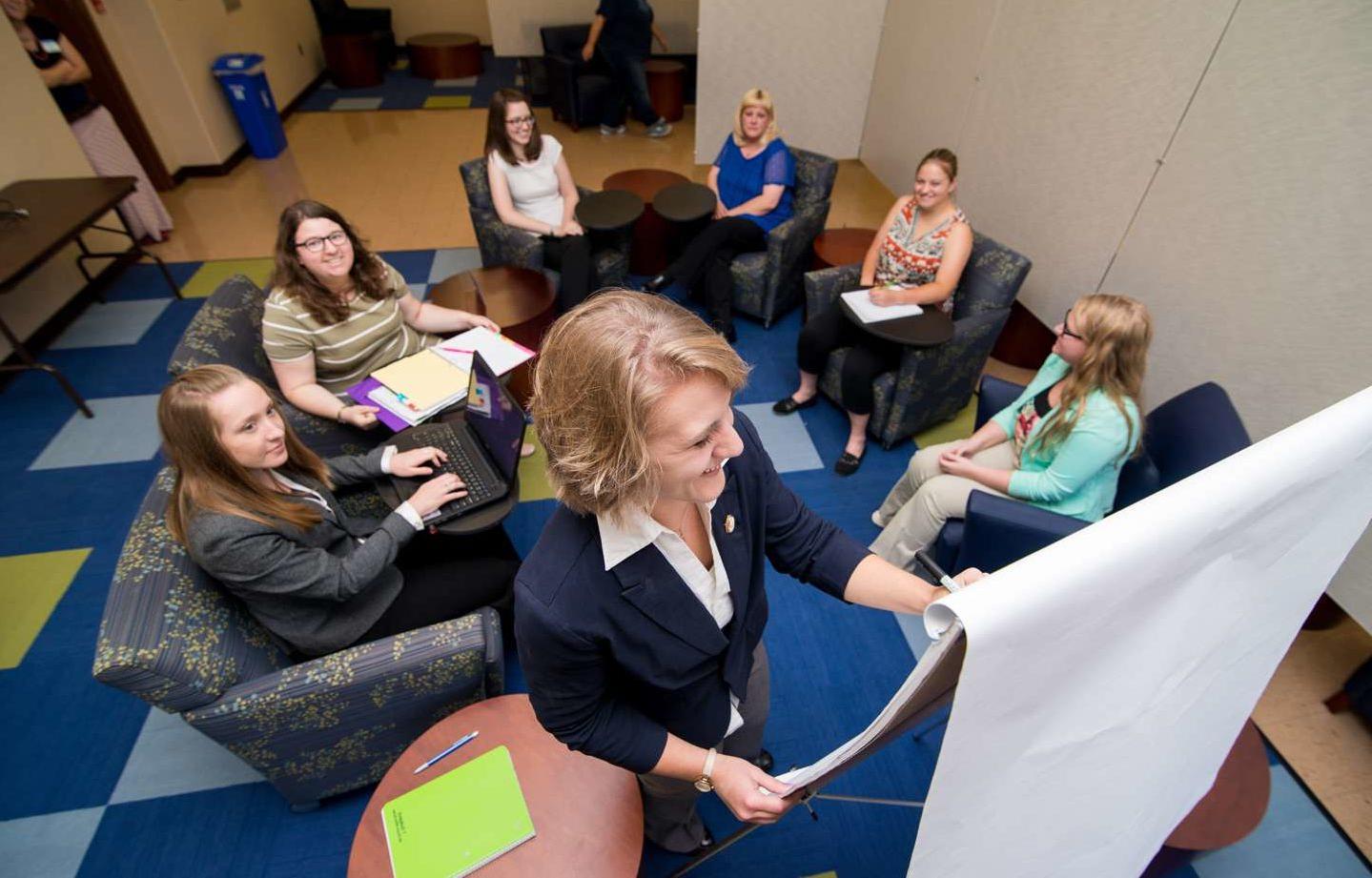 A student writing on a flip chart during a meeting with other students in the Woods Student Center.